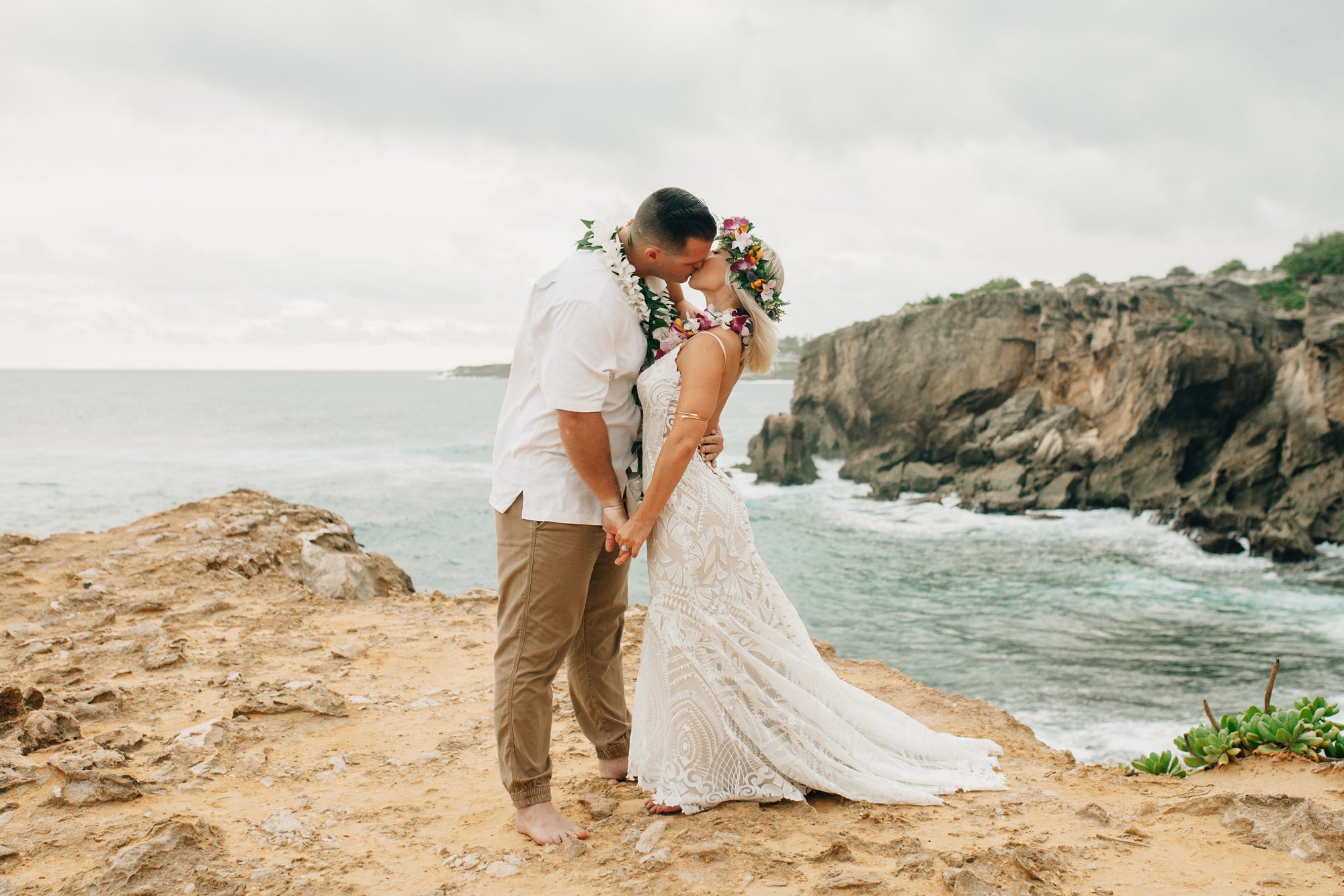 Eloping couple share their first kiss as husband and wife on a cliff at Shipwreck Beach on Kauai.