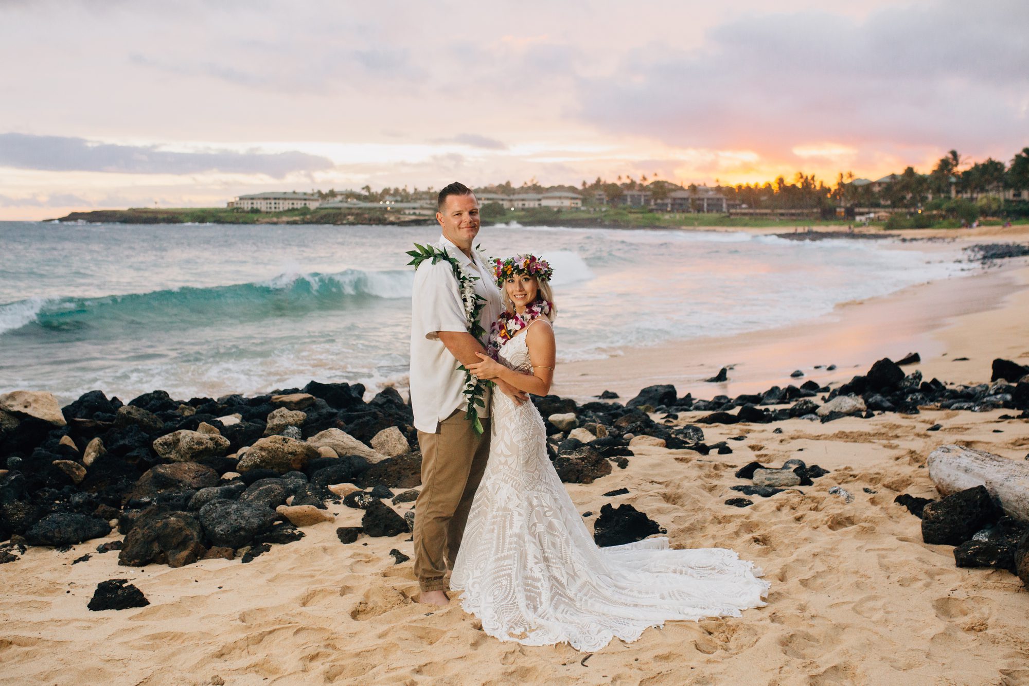 Bride and groom pose in front of the rocky Shipwreck Beach sunset.