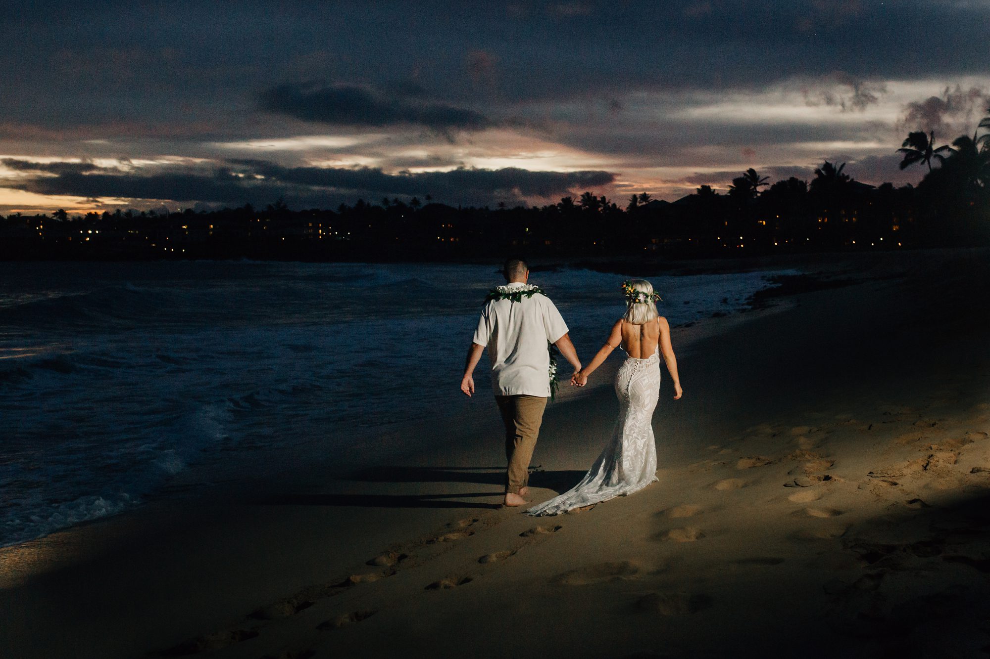 Bride and groom walking on Shipwreck Beach at dusk.