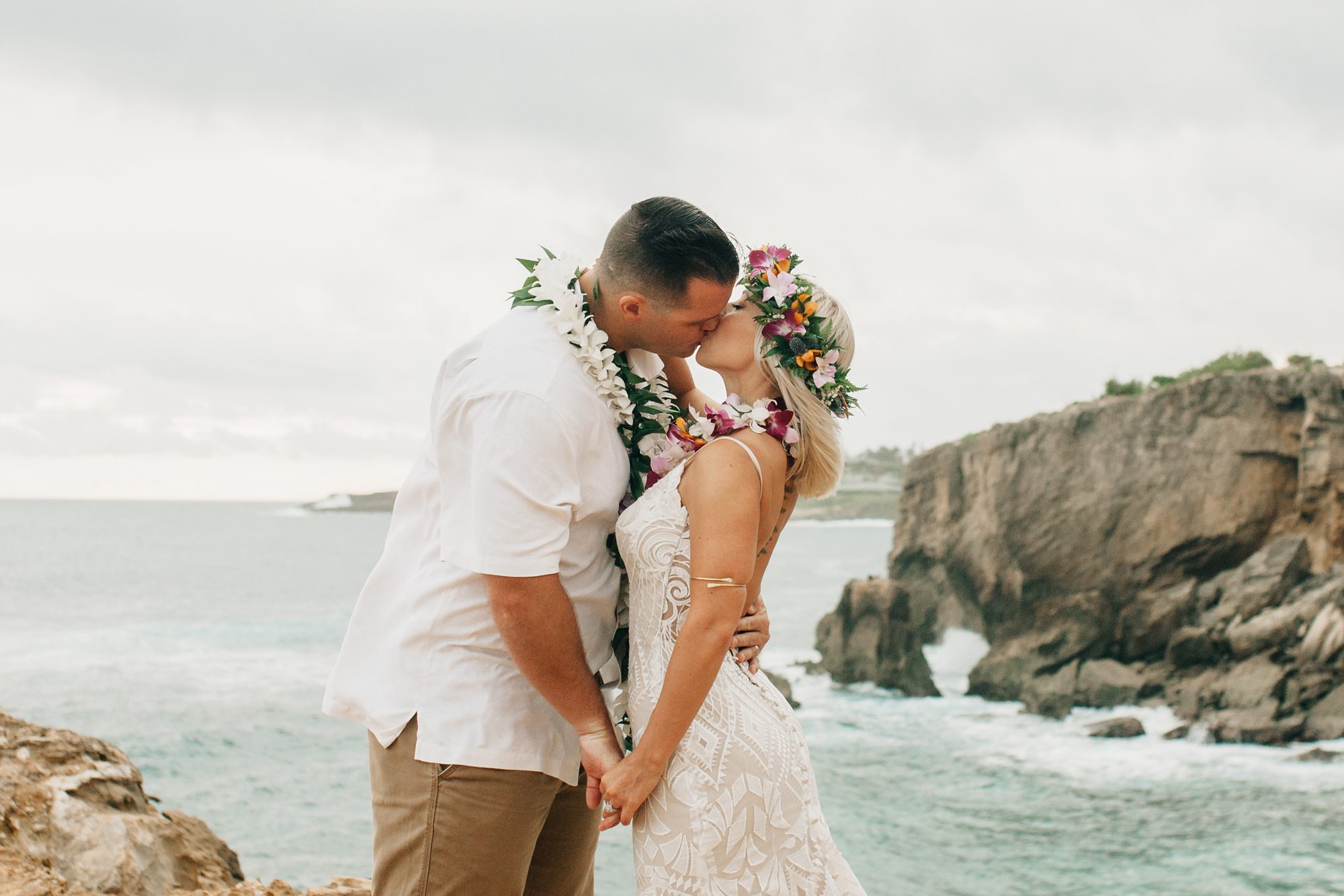 Bride and groom share their first kiss as a married couple. The ocean and cliffs are in the background.